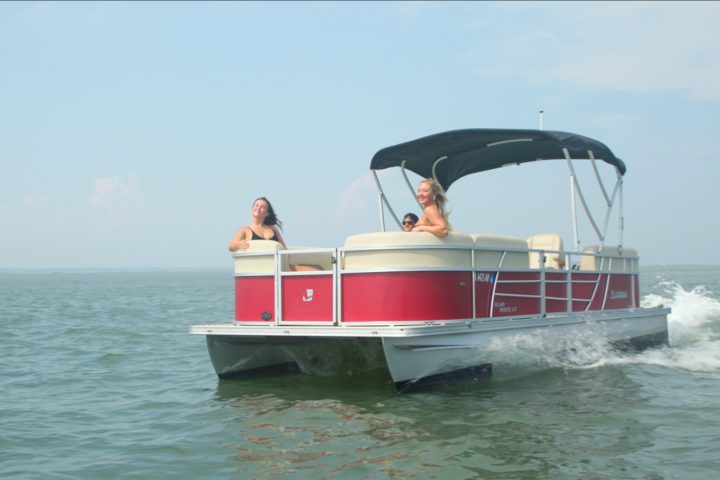 Pontoon boat with three people on open water under clear sky.