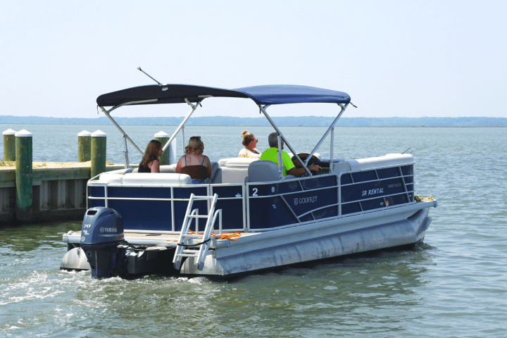 People on a pontoon boat near a dock on a calm lake.