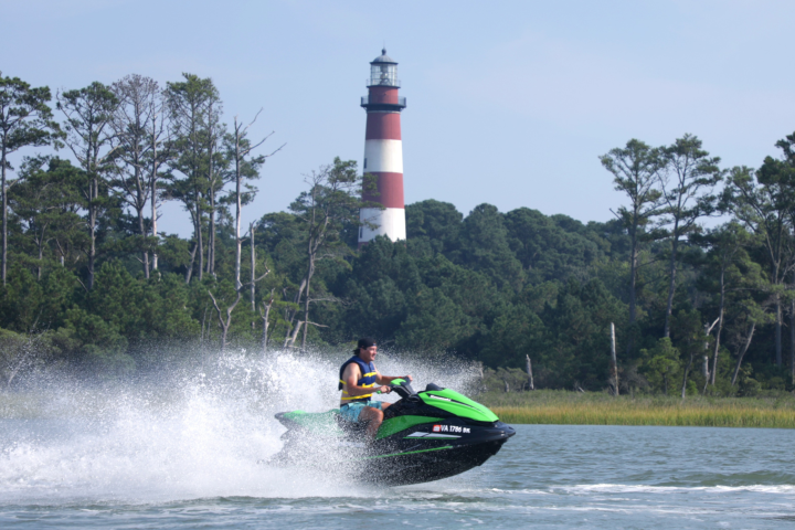 Person jet skiing with a lighthouse and trees in the background.