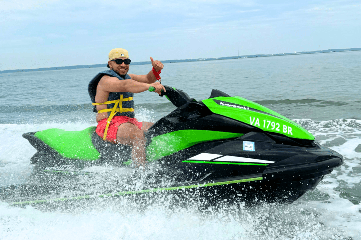 Man riding a green jet ski on the ocean, giving a thumbs-up.
