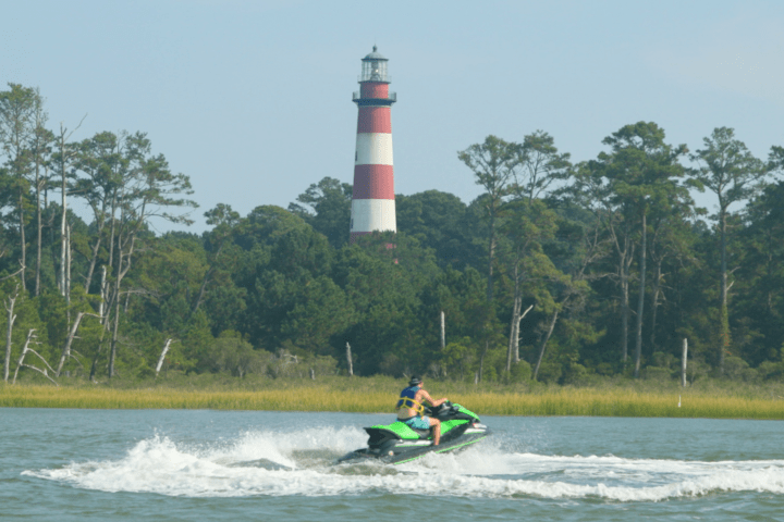 Person on jet ski in front of red and white lighthouse with trees.