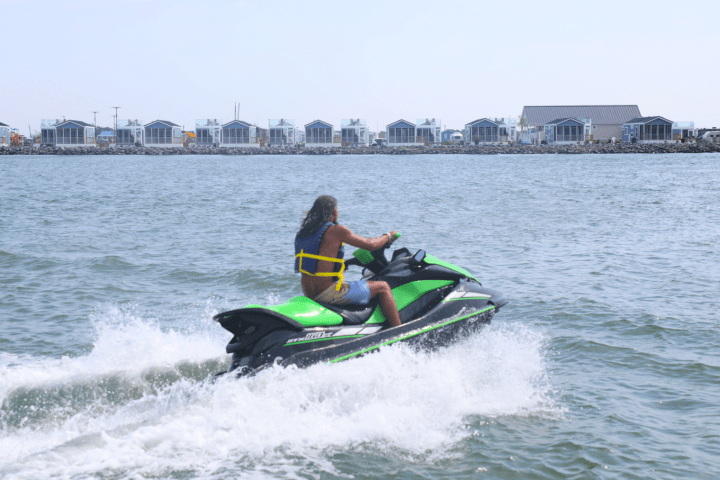 Person on a green jet ski riding on water near a row of houses.