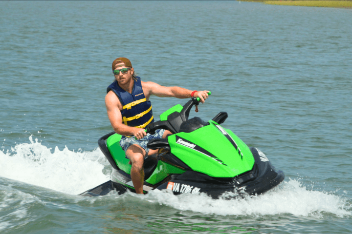 Person riding a green jet ski on a lake, wearing a life vest.