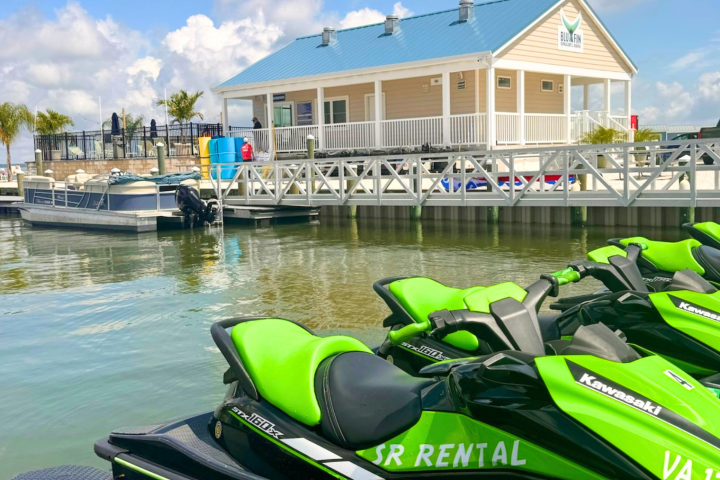Green jet skis by dock with beige building and boats in the background.