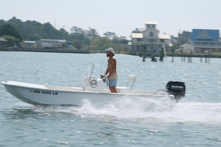 Man steering a small motorboat on a sunny day near the shore.