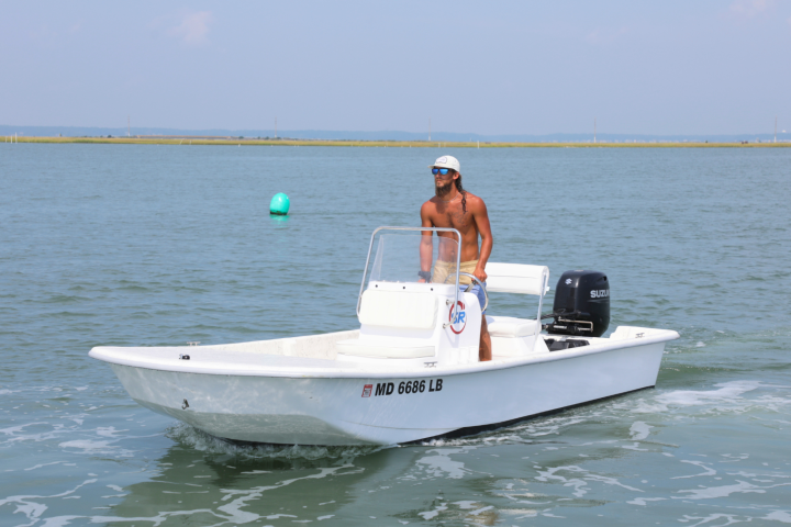 Man steering a small white motorboat on a calm body of water.