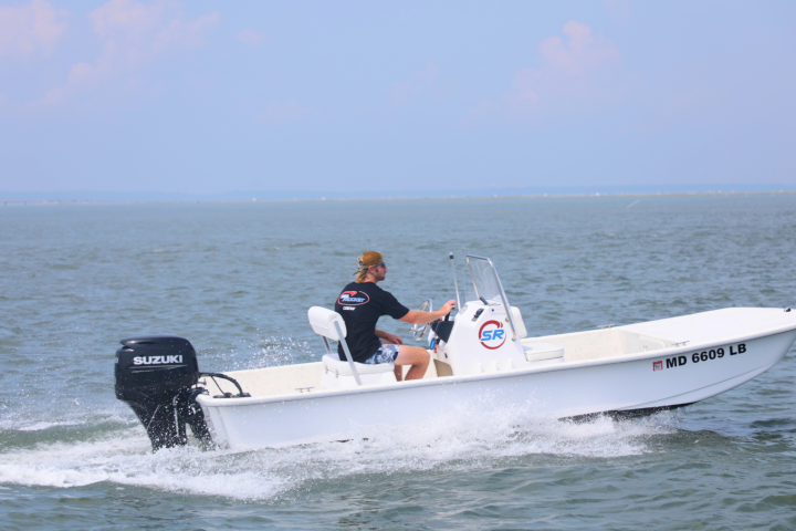Man driving a small motorboat on open water under a clear sky.