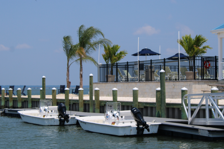 Two small boats docked near a waterside restaurant with palm trees.