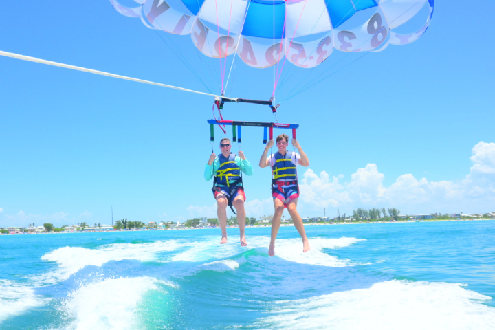 Two people parasailing over the ocean with a colorful parachute and clear blue sky.