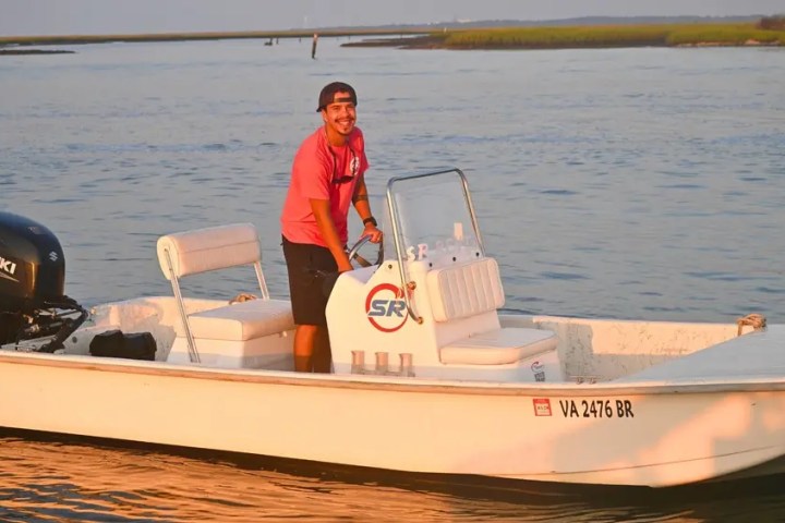 Man smiling on a small white boat on the water at sunset.