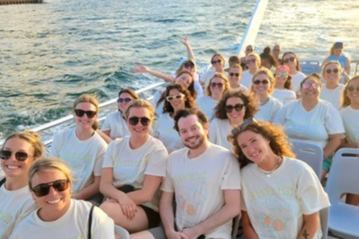Group of people wearing white shirts sitting on a boat with water in the background.