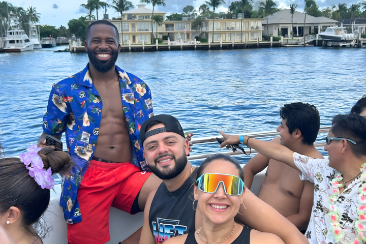 Group of people smiling and relaxing on a boat with water and waterfront houses in the background.