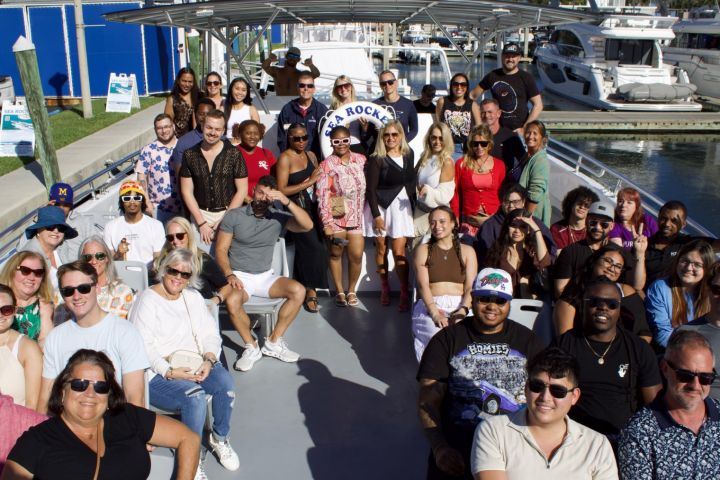 Group of people on a docked tour boat, smiling and posing for a photo on a sunny day.