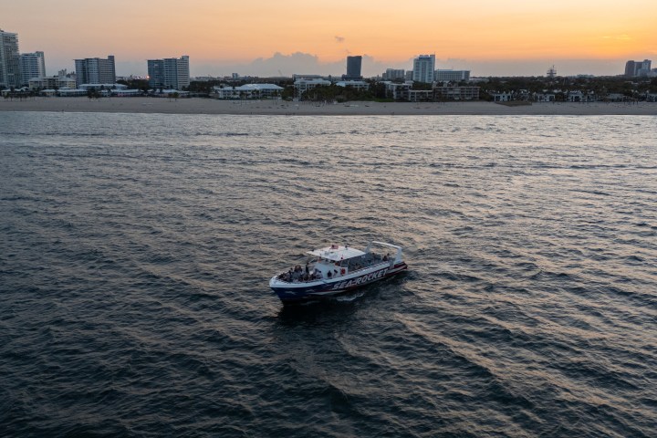 Boat on water with city skyline at sunset in the background.