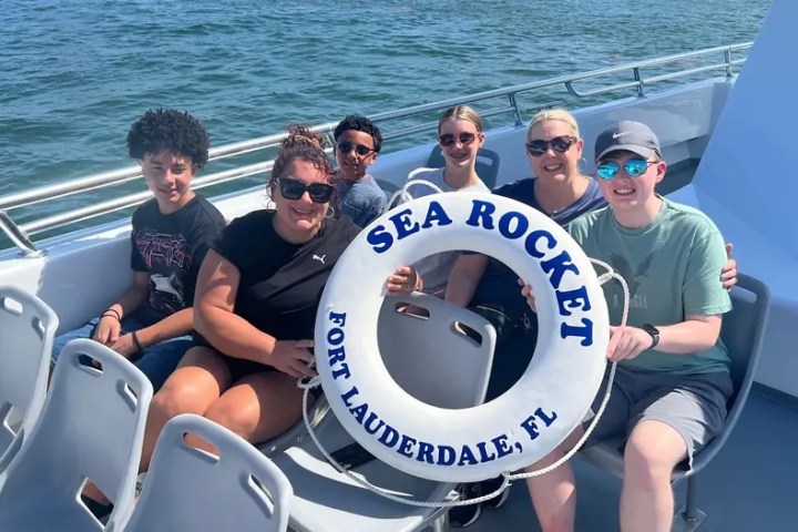 Group of five people on a boat holding a life ring labeled 'Sea Rocket, Fort Lauderdale, FL'.