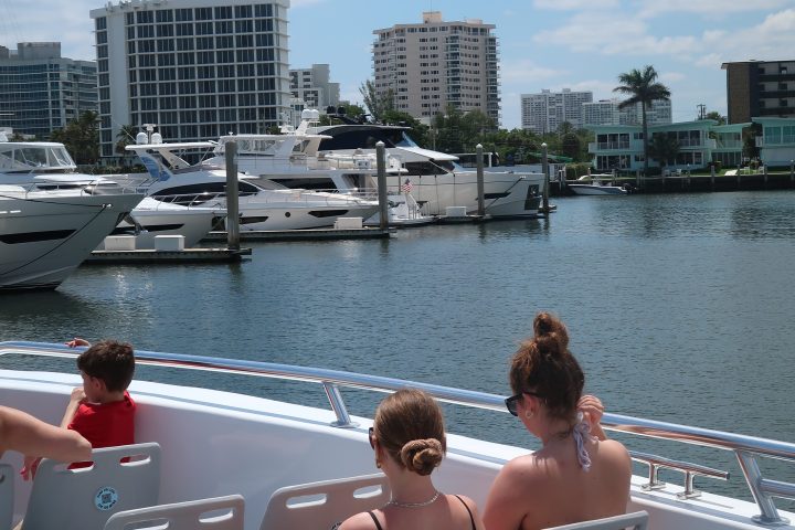 People sitting on a boat with a cityscape and boats in the background.