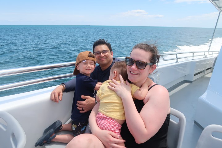 Family of four smiling on a boat with ocean in the background.