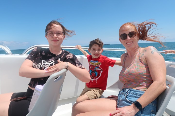 Three people on a boat smiling, with ocean and clear sky in the background.
