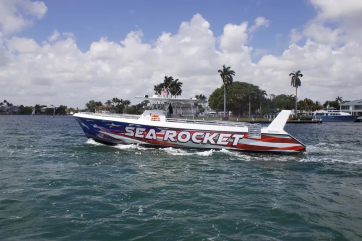 Boat named 'Sea Rocket' on water, painted with American flag design, palm trees in background.