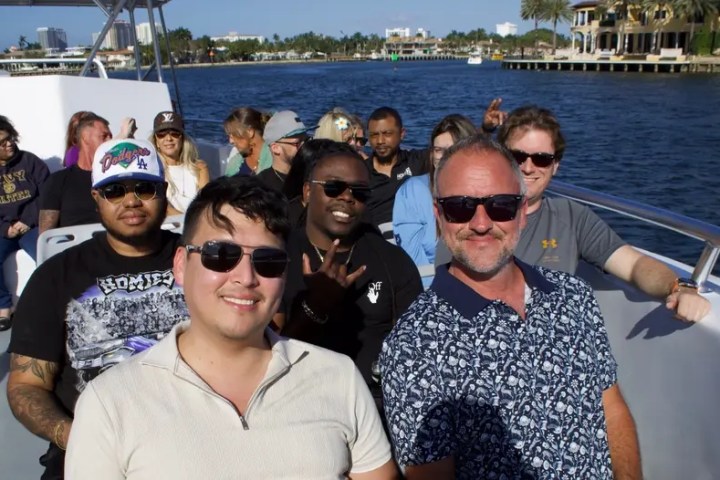 Group of people sitting on a boat, smiling, with water and city in the background.