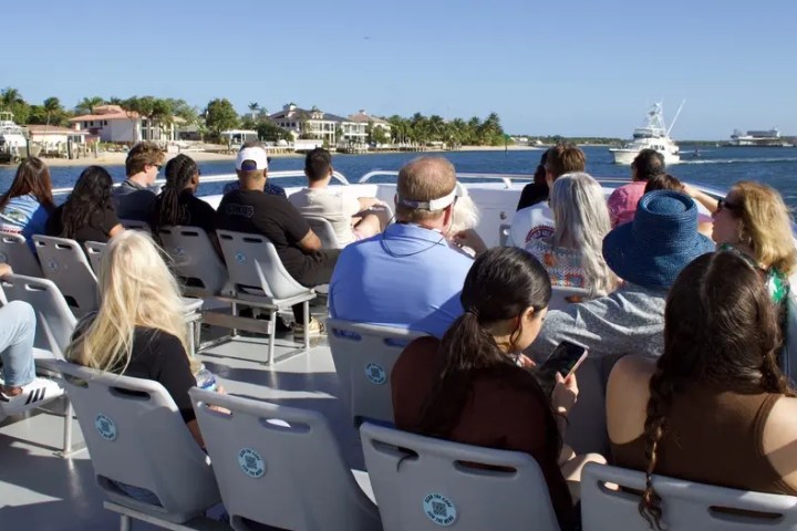 People seated on a boat enjoying a sunny day with waterfront homes in the background.
