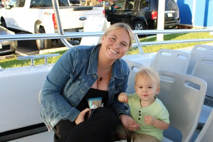 Woman and child sitting on outdoor seating with parked cars in background.