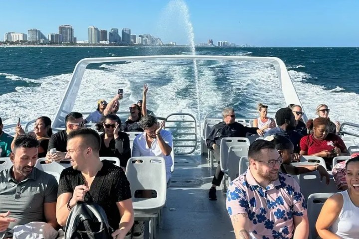 People enjoying a sunny boat ride with city skyline in the background.