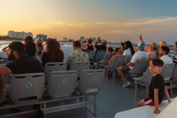 People on a boat watching sunset with city skyline in the background.