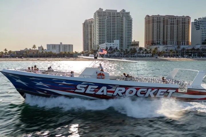Boat named Sea Rocket speeds on water near a cityscape with tall buildings.