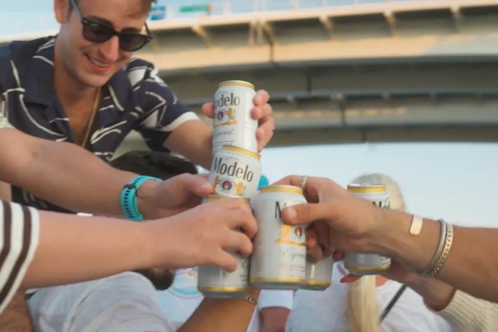 Group of people toasting with Modelo beer cans outdoors.