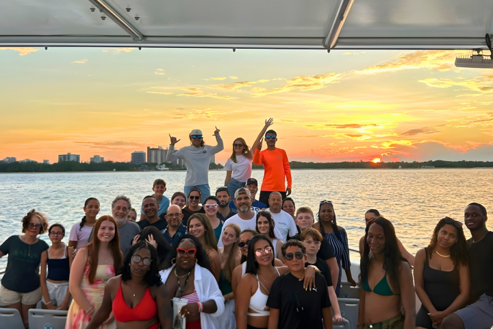 Group of people on a boat at sunset, with city skyline in the background.