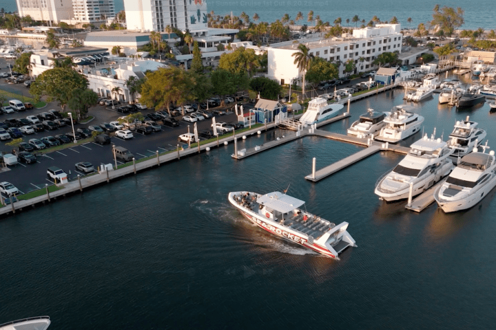 Aerial view of a marina with yachts and a moving speedboat in a coastal city.