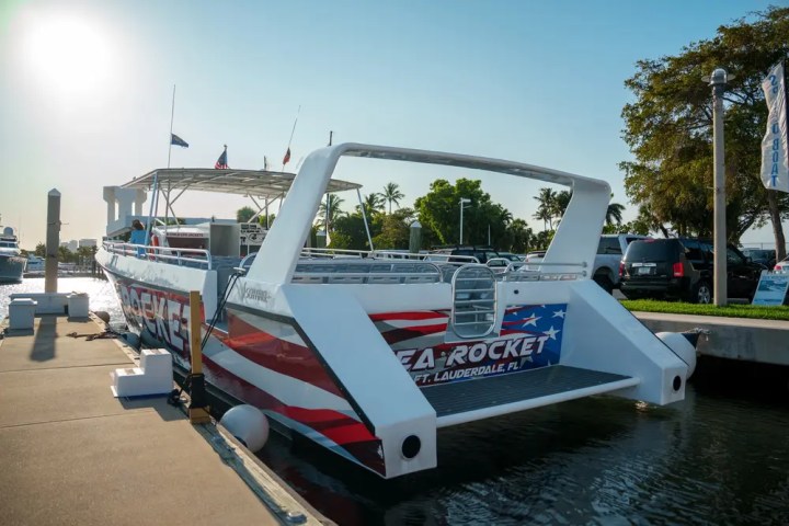 Boat named 'Sea Rocket' docked with American flag design, sunny day, parked cars and trees in background.