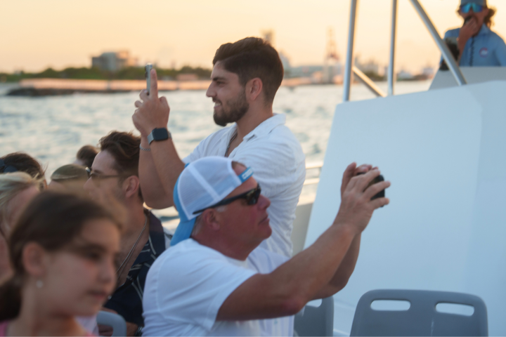 People on a boat taking photos, with sunset and water in the background.