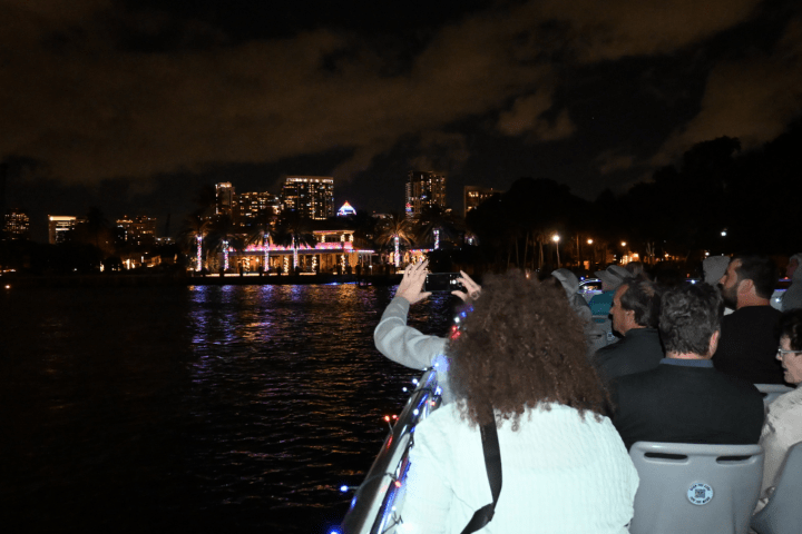 People on a boat at night with cityscape and lit building in background.