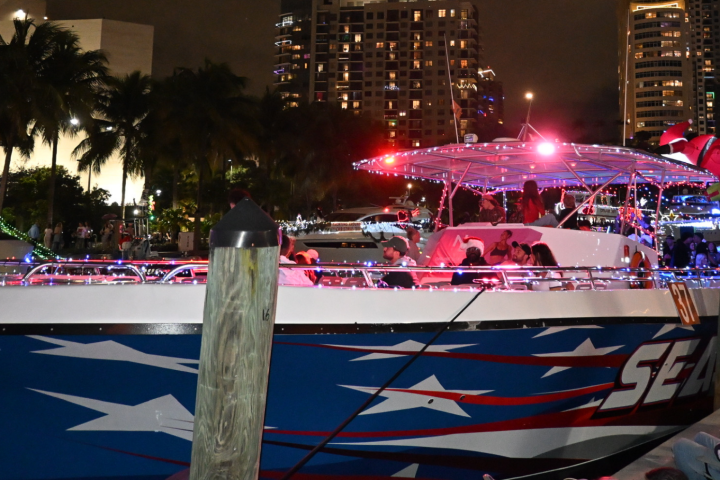 People on a brightly lit boat at night with city skyline in background.