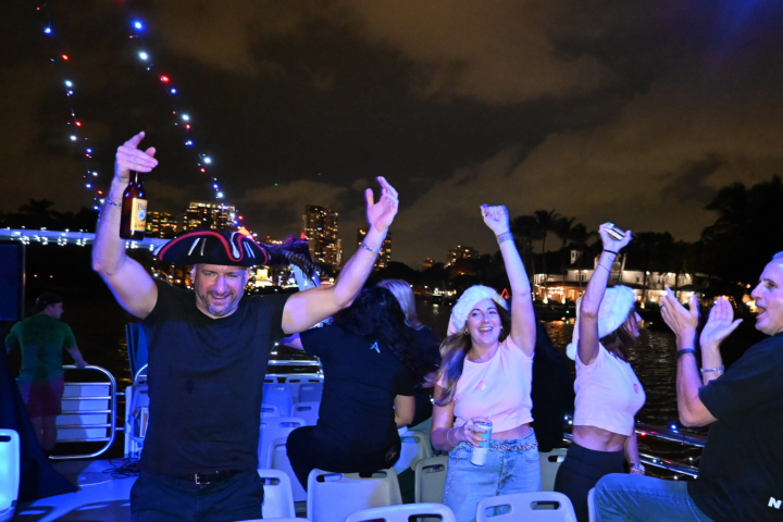 People dancing and celebrating on a boat at night with city lights.