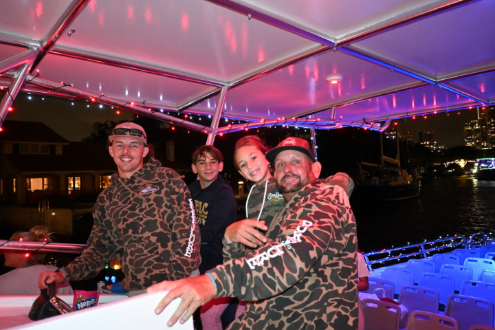 Four people smiling on a decorated boat at night.