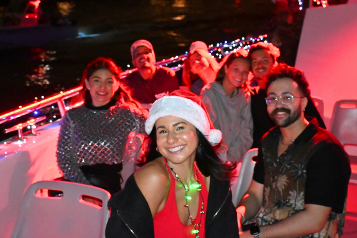 Group of people on a decorated boat at night, one wearing a Santa hat.