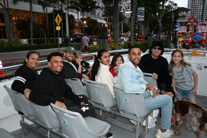 People seated on a boat, smiling, near a waterfront with trees and buildings.