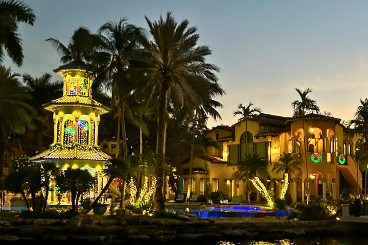 Illuminated gazebo and villa with palm trees at sunset.