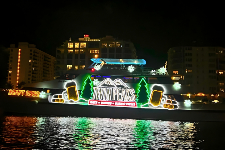 Boat with neon Twin Peaks sign and trees, night view on water.