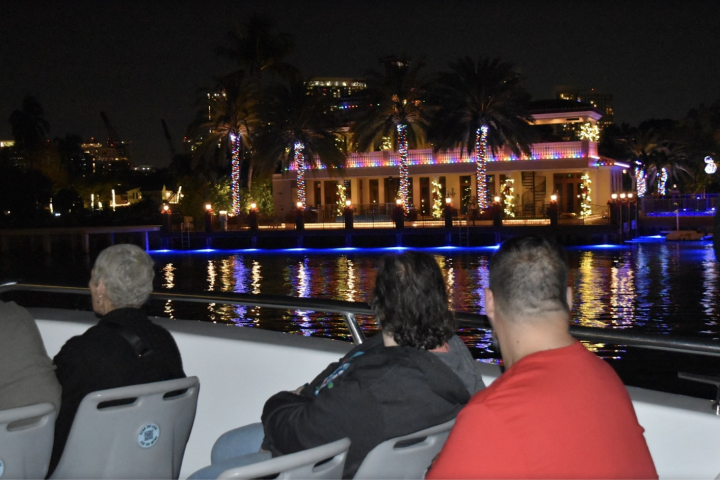 People on a boat at night with a building adorned with festive lights in the background.