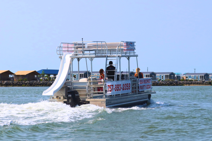Pontoon boat with water slide and passengers in open water near shore.