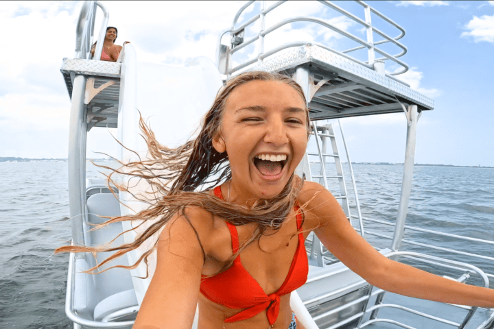 Woman in red swimsuit laughing on a boat slide, ocean in background.