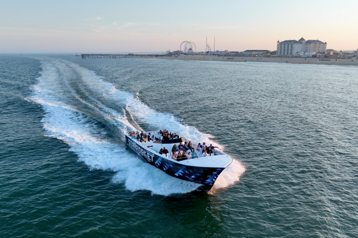 Speedboat with passengers on open water near coastline and city buildings.