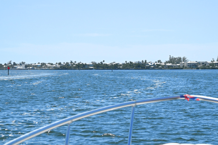 View from boat of calm water with distant coastline and houses on a sunny day.