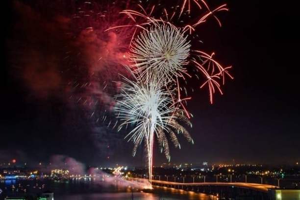 Fireworks exploding over a bridge, illuminating the night sky and reflecting on the water below.