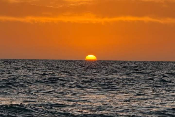 Sun setting over the ocean with orange sky and calm waves.