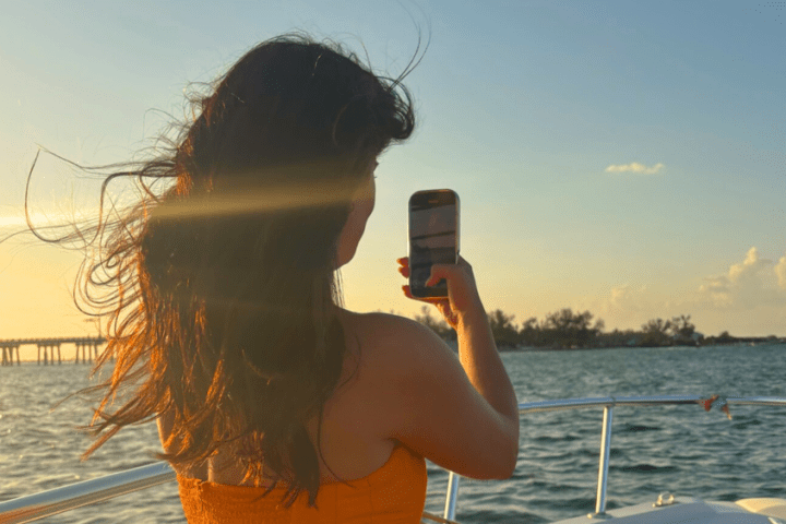 Woman on boat taking photo of sunset over the sea.